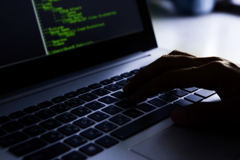 A closeup shows a hand typing on a computer keyboard in a dimly lit room.