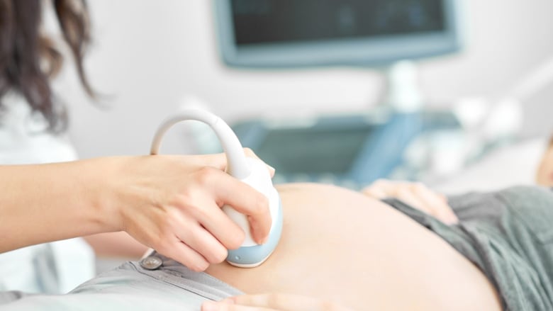 Someone in a lab coat gives a pregnant person an ultrasound.