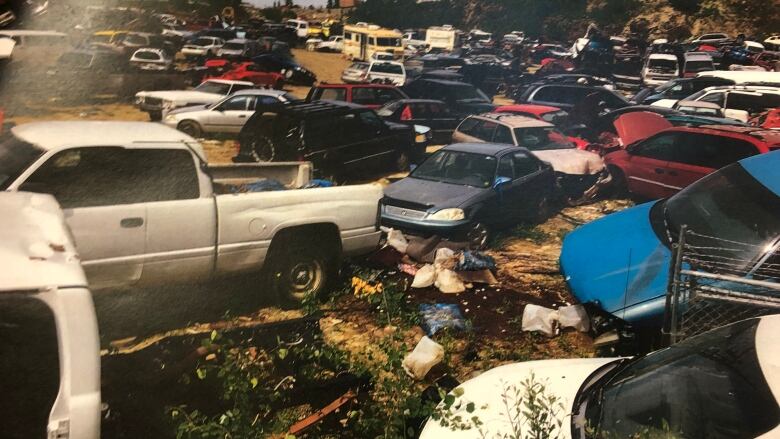 Dozens of vehicles parked on a lot with garbage on the ground.