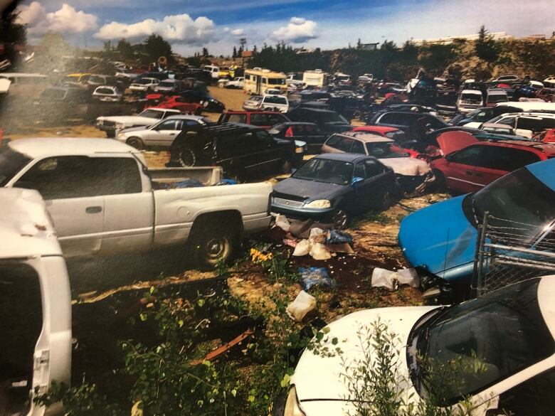 Dozens of vehicles parked on a lot with garbage on the ground.