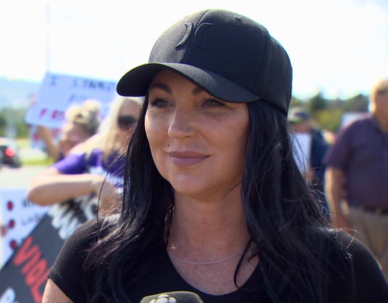 A woman with dark hair wearing a black baseball hat looks to the left of the image.