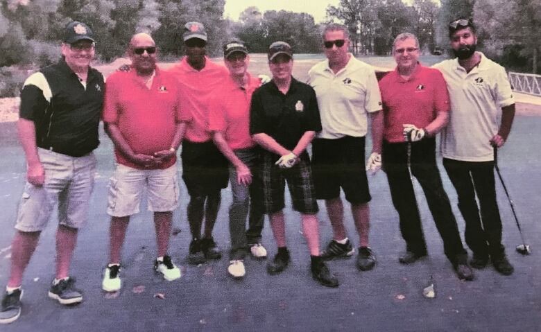 Eight men stand beside each other, posing on a golf course.