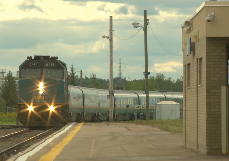 A green train on a track with the words Via Rail written on the front. It is driving up toward a station. 