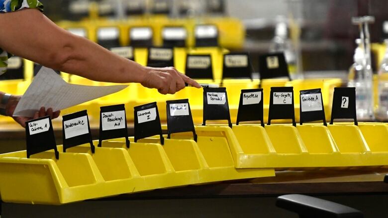 A worker organizes bins labelled with the names of candidates into which special ballots from national, international, Canadian Forces and incarcerated electors will be placed and counted, at Elections Canada's distribution centre in Ottawa on election night of the 44th Canadian general election, on Monday, Sept. 20, 2021.