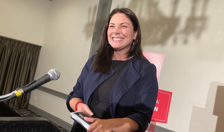 A woman smiling in front of a microphone. She is holding a notebook in her hands.