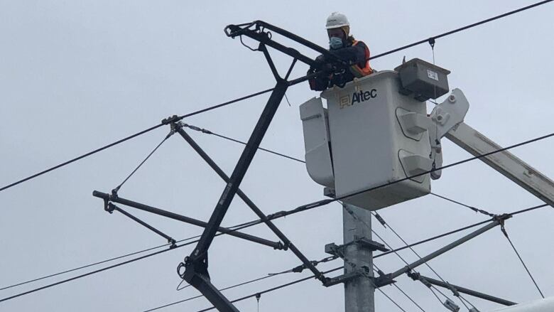 A worker in a bucket truck works on a power system above a public transit train.