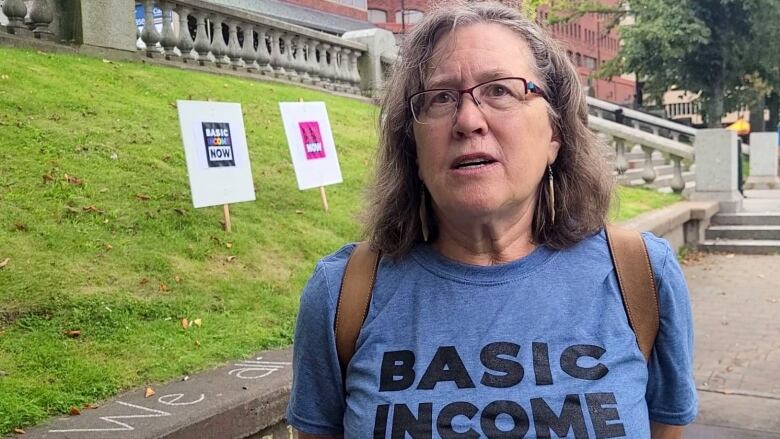 A woman with glasses stands outside near grass.