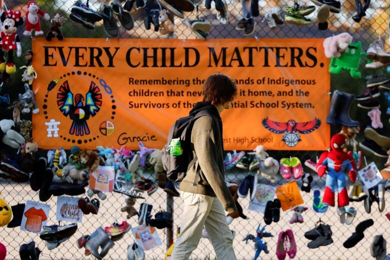 a person walks by an every child matters sign on a fence.