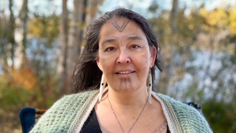 Woman showing her tattoos and with trees in the background.