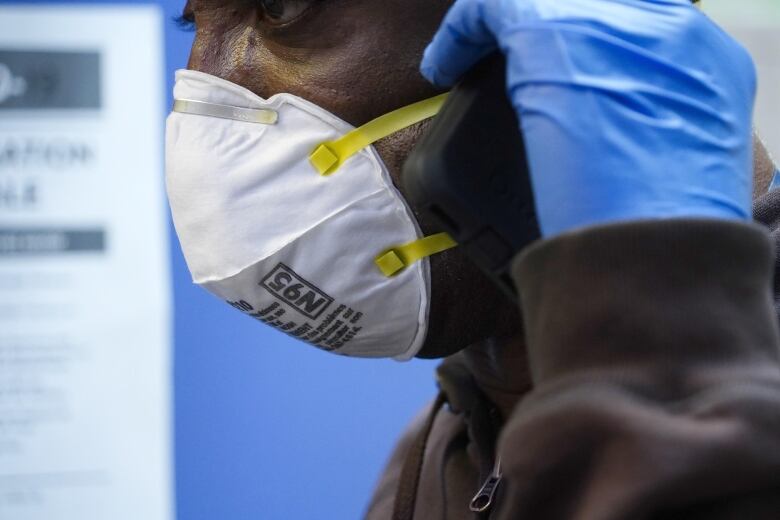 A person wearing blue latex gloves and a white N95 mask.