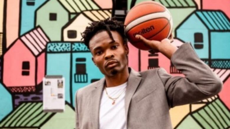 A man holding a basketball stands in front of an outdoor wall mural. 