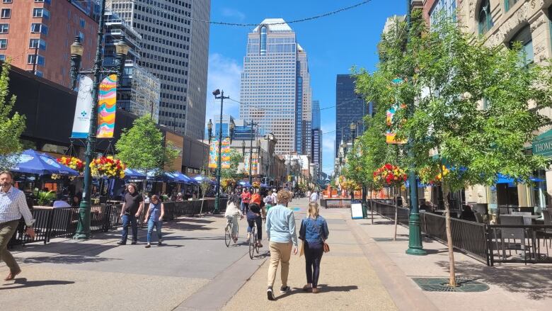 People walk down the street on a bright sunny day. Tall downtown buildings can be seen around them.