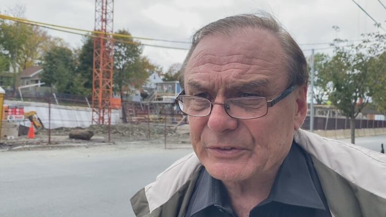 A man with glasses is shown in front of a property under construction.