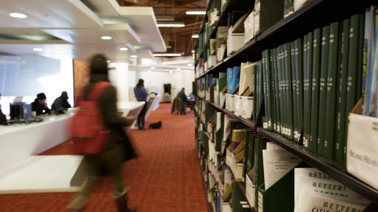 Blurry images of library patrons are seen alongside a row of bookshelves.