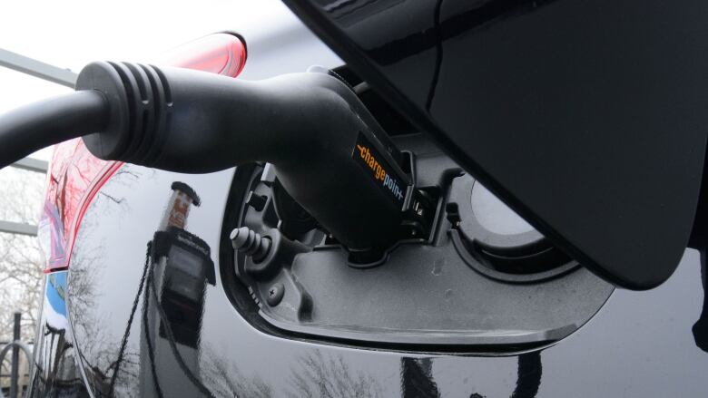 A charging handle is inserted into the port of a white electric car.