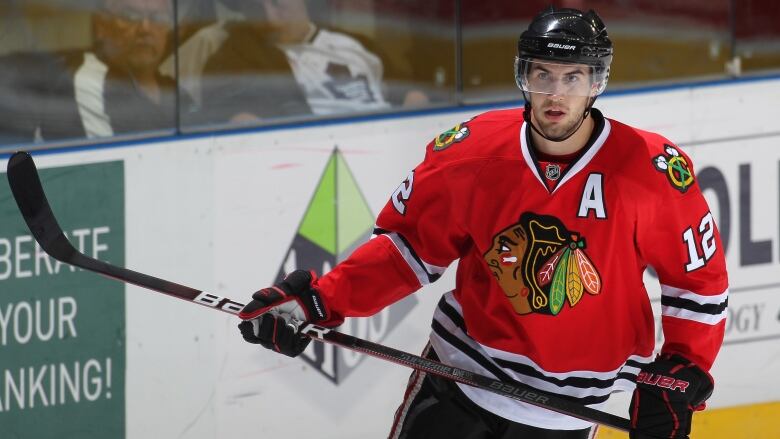 A man in a red hockey jersey and black helmet holding a hockey stick. 