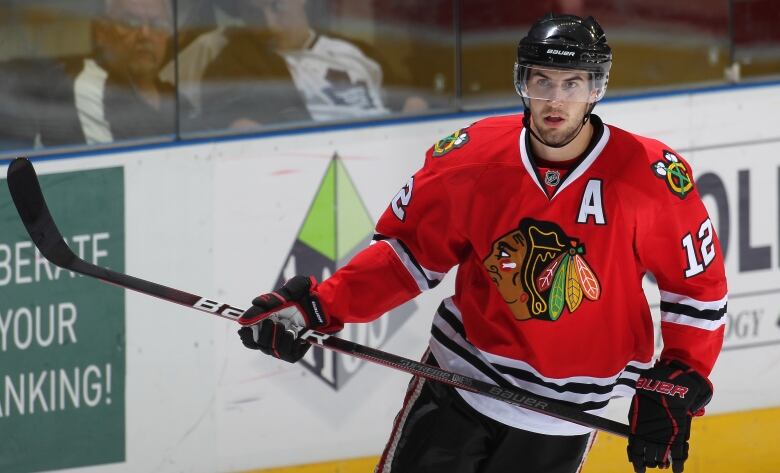 A man in a red hockey jersey and black helmet holding a hockey stick. 