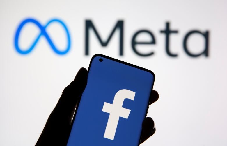 A smartphone with Facebook's logo is seen in front of displayed Facebook's new rebrand logo Meta.