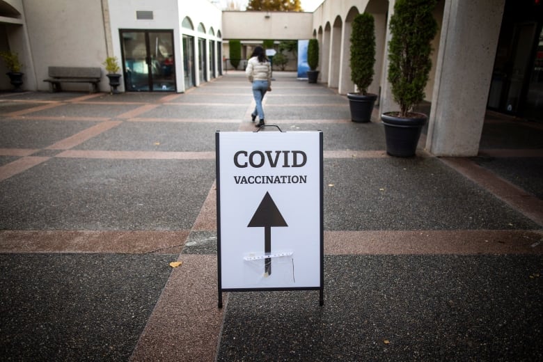 A sign pointing upwards says 'COVID Vaccination' in an outdoor space.