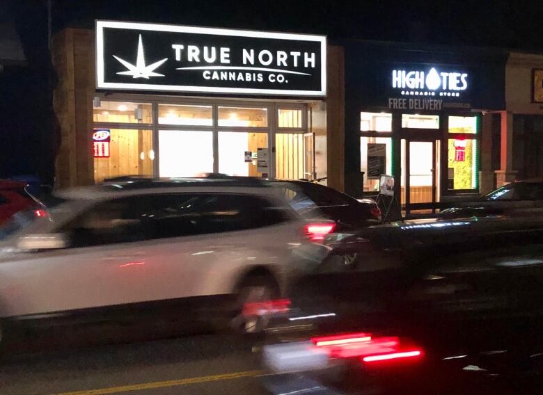 A nighttime photo of two retail cannabis shops side-by-side, with signs saying 'True North Cannabis Co.' and 'High Ties Cannabis Store.'