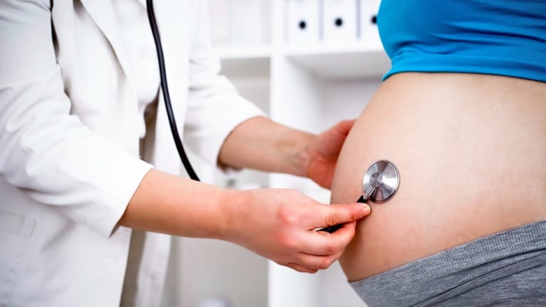 A health care provider holds a stethoscope up to the abdomen of a pregnant patient