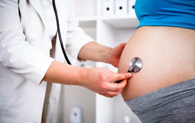 A health care provider holds a stethoscope up to the abdomen of a pregnant patient