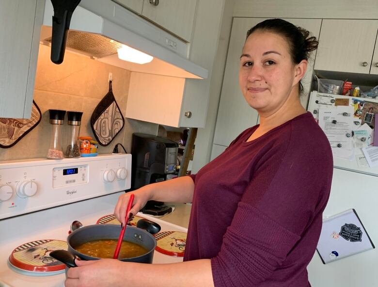 A woman stands at a stove, stirring a pot of soup.