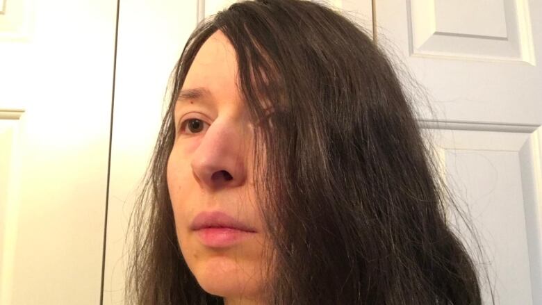 Close up portrait of a woman in front of a closet door and with her long dark hair hiding half of her face