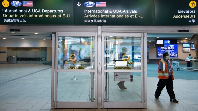 An airport worker in a high-vis vest walks past an airport entrance at Vancouver International Airport.