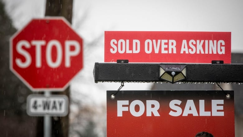 A real estate sign that reads 'SOLD OVER ASKING' just atop a sign that reads 'FOR SALE'.