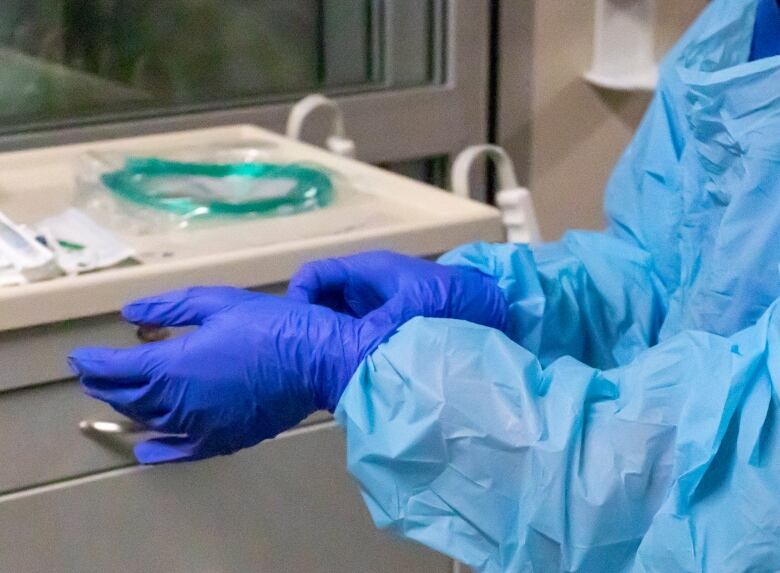 Arms and hands of someone wearing plastic blue hospital gown and blue protective gloves.