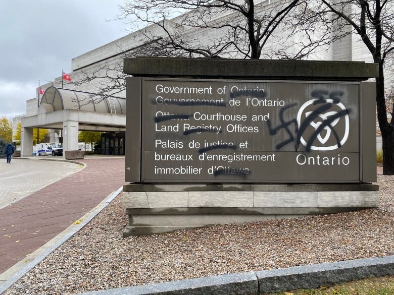 A sign for a provincial courthouse is vandalized with a swastika.