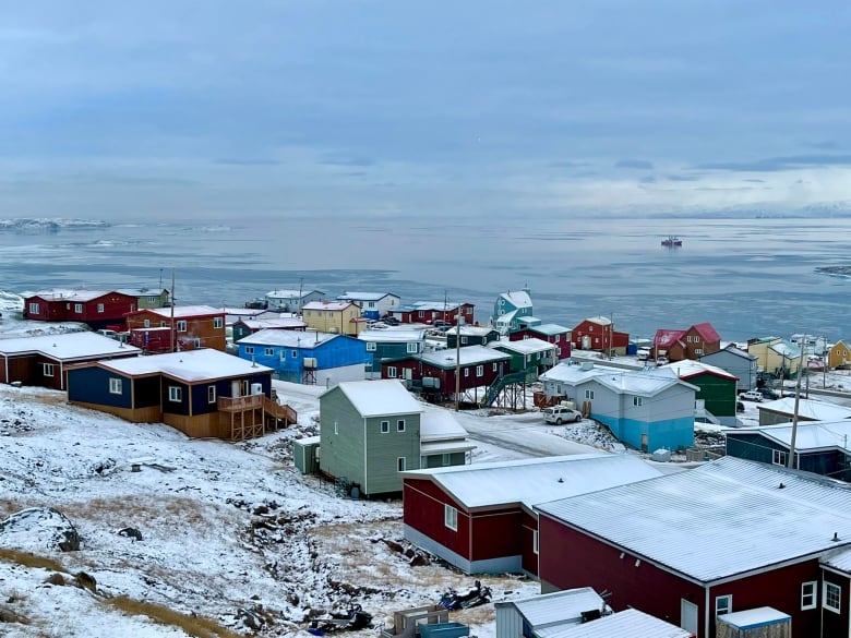 Rows of houses sit on snow with water in the background.