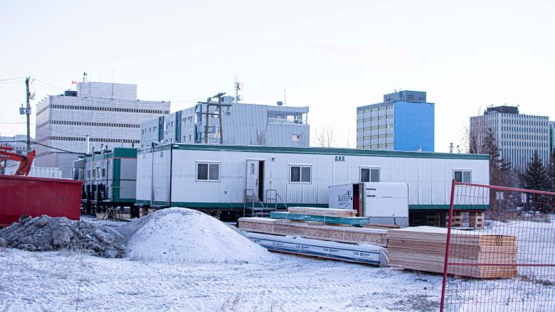 A building sits on snow, surrounded by construction materials and fencing.