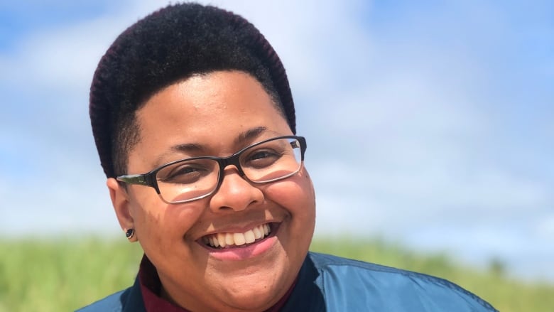 A Black woman smiling wearing glasses and a wine shirt and blue jacket.