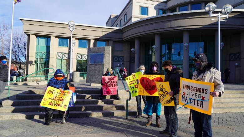 Protesters with signs against a pipeline stand outside a municipal building.