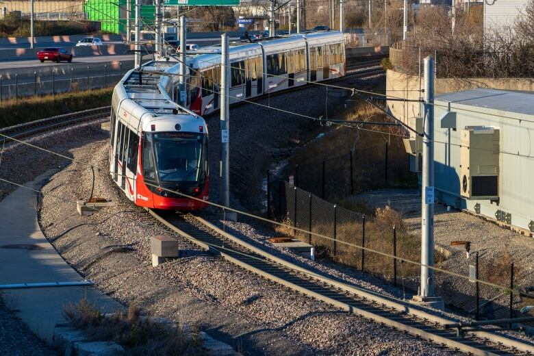 A red and white light rail train rounds a bend in the sunlight.