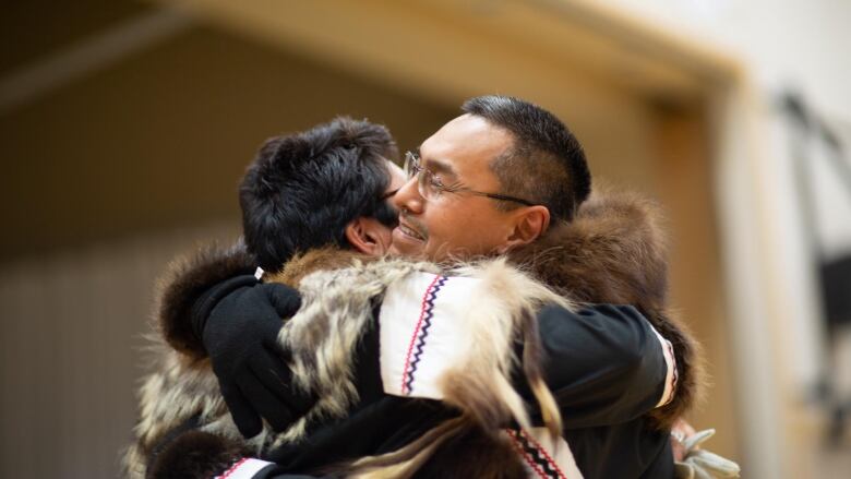 A man and woman share a big arms-over-shoulders hug. The man is smiling.