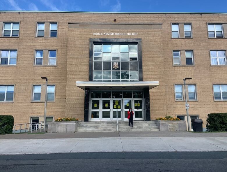 A person in a red jacket is walking down the stairs from a beige brick building.