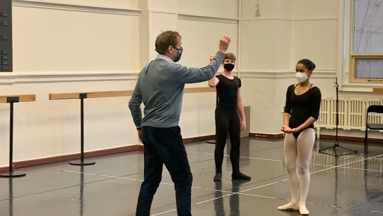 A ballet instructor is seen giving directions to young dancers in a studio.