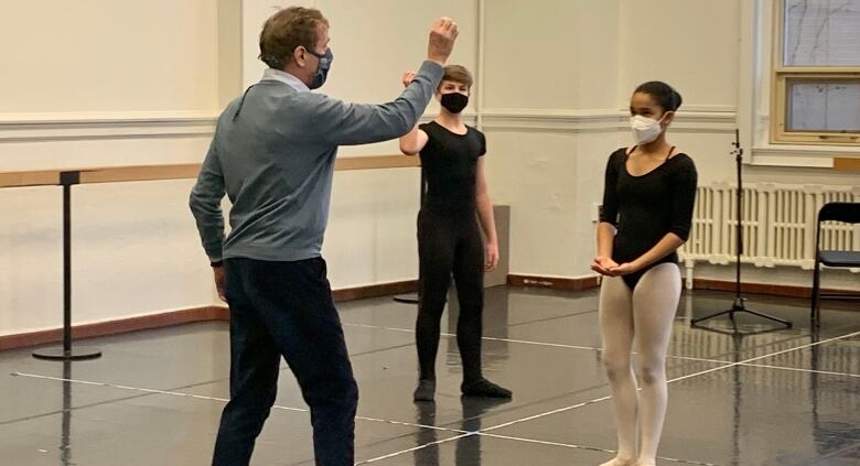 A ballet instructor is seen giving directions to young dancers in a studio.