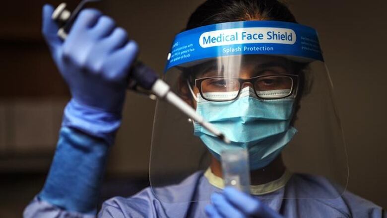 A lab scientist wearing full protective gear holds a device over a sample tube.