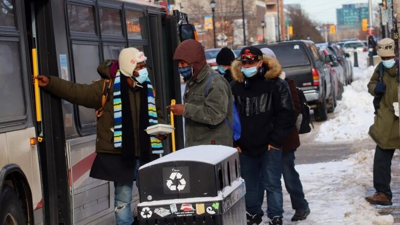 People wearing masks board a bus on a winter day.