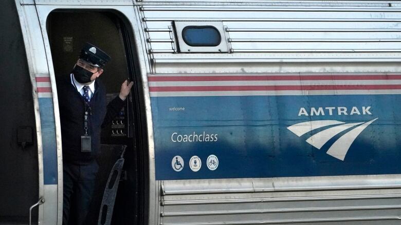 A man wearing a mask stands in the door of a train marked 'Amtrak'.