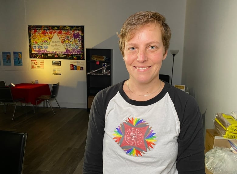 A woman stands in a dimly lit room smiling at the camera. 