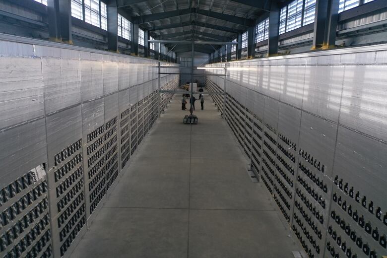 A picture inside a bitcoin mining facility shows long walls on either side of a concrete floor. The walls are filled with tiny computers.