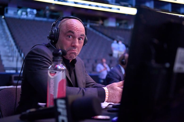 A man in front of a screen with black headphones on.