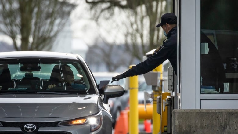 An officer at a border crossing reaches out to get someone's documents from a car window.