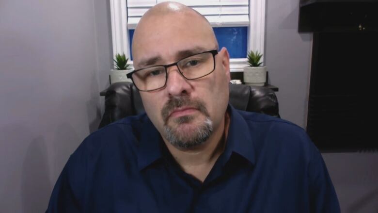 A bald man wearing a dark blue shirt and glasses