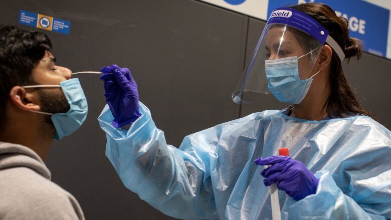 A woman wearing a mask, gloves and other protective gear carries out a nose swab on a man.